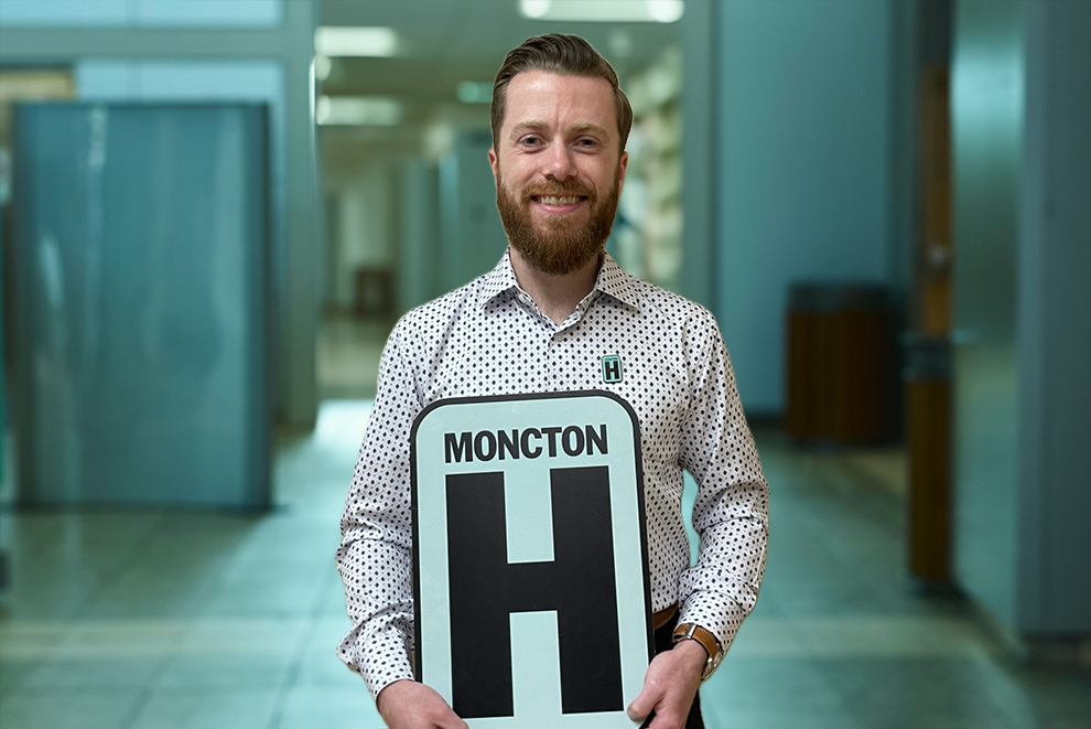 Aaron Headshot Holding Moncton H logo