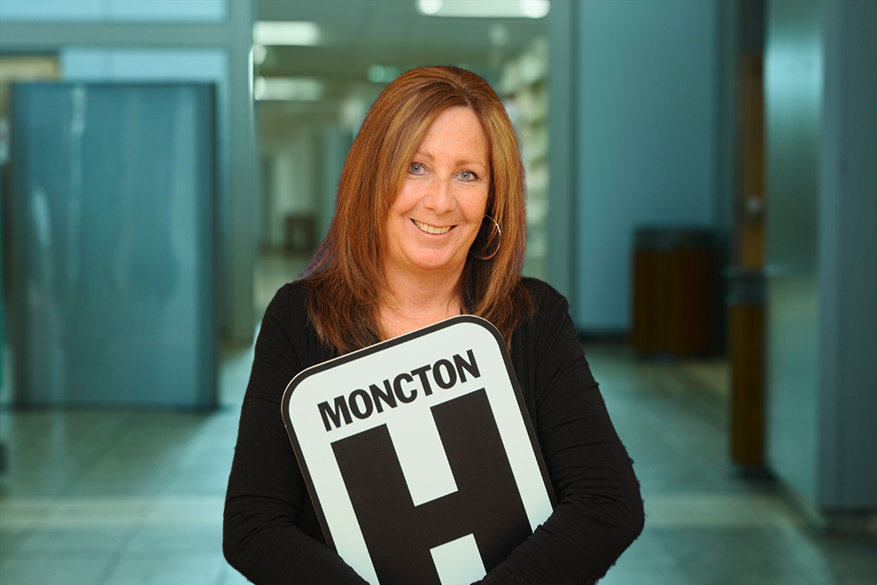 Julie Headshot Holding Moncton H logo