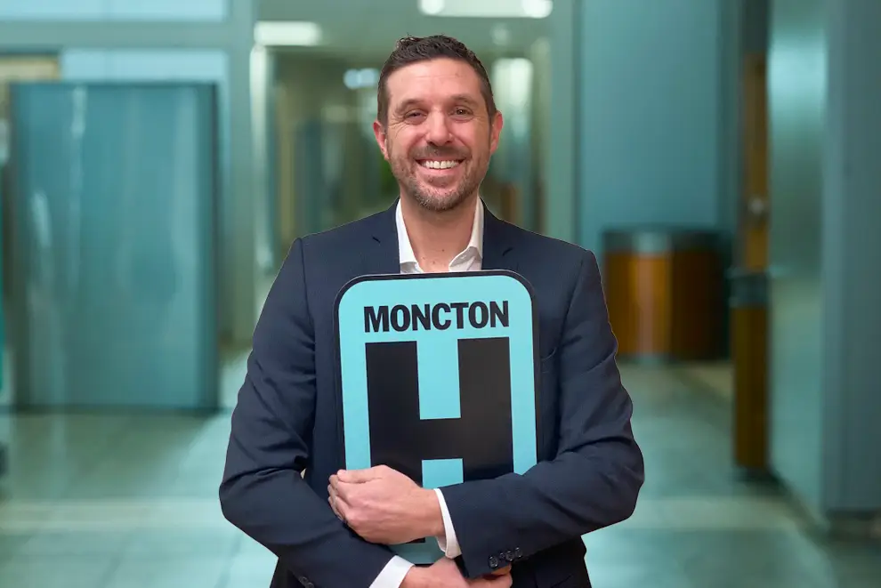 Marc Belliveau Holding H Sign and Smiling at camera